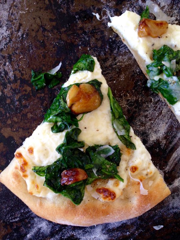 Slice of Ricotta Spinach Pizza with Roasted Garlic Cloves on a Distressed Cookie Sheet