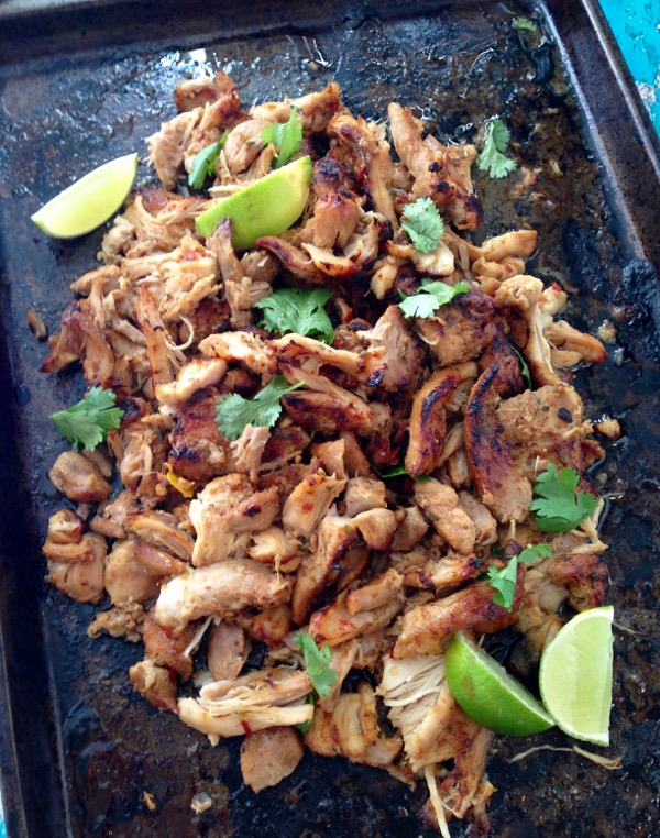 Black cookie sheet with shredded chicken carnitas and limes