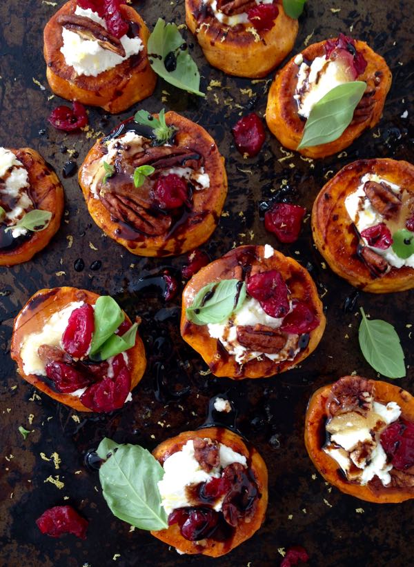 A Black Tray of Sweet Potato Rounds Appetizers Topped with Goat Cheese, Candied Walnuts, Cranberries & Balsamic Glaze