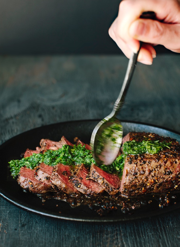 Sliced peppercorn crusted steak drizzled in chimichurri sauce in a cast iron skillet