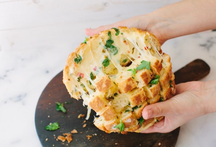 Hands Holding a Cheesy Garlic Pull Apart Bread Over a Wooden Board