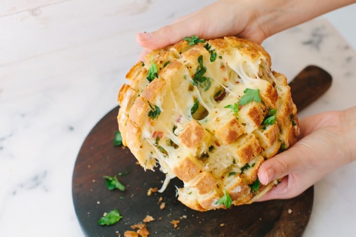 Hands Holding a Cheesy Garlic Pull Apart Bread on Top of a Wooden Board