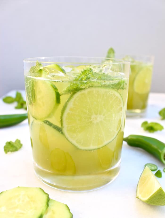  Mojito glasses on a white table with lime, cucumber slices and jalapeno