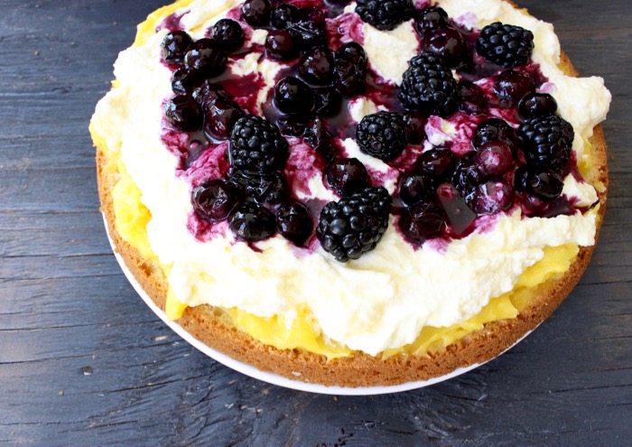 First Layer of Lemon Olive Oil Cake Covered with the Lemon Curd, Mascarpone Filling and Berry Sauce on a Rustic Table