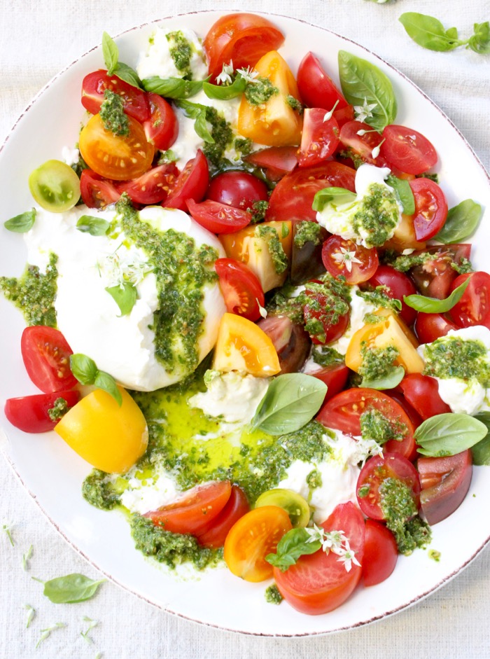Colorful Heirloom Tomato Burrata Caprese Salad on a white Platter with Drizzles of Basil Pesto
