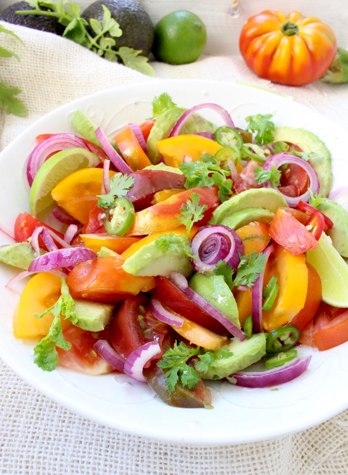 Colorful heirloom tomato avocado salad with purple onions and lime dressing in a white bowl.