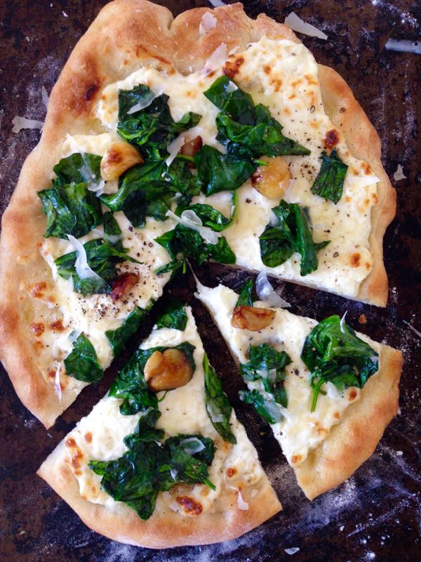 Sliced up pizza Bianca with Ricotta and Spinach on a distressed cookie sheet.