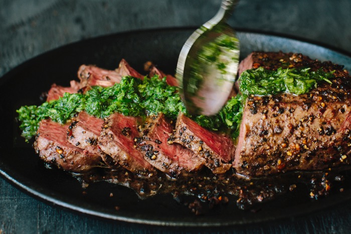 Sliced steak drizzled in chimichurri sauce in a cast iron skillet