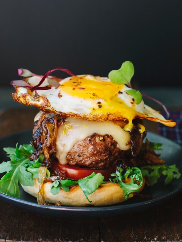 Breakfast Burger with a Fried Egg on Brioche Bun with Caramelized Onions and Arugula on a Cutting Board