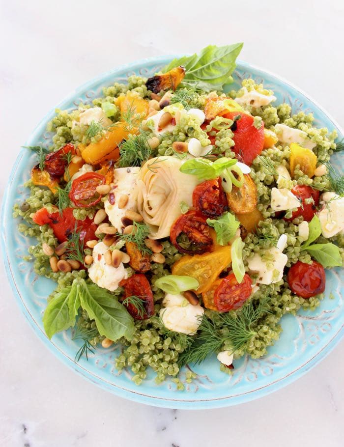 Mediterranean quinoa salad dressed in basil pesto with roasted tomatoes, peppers and artichokes on a blue serving platter